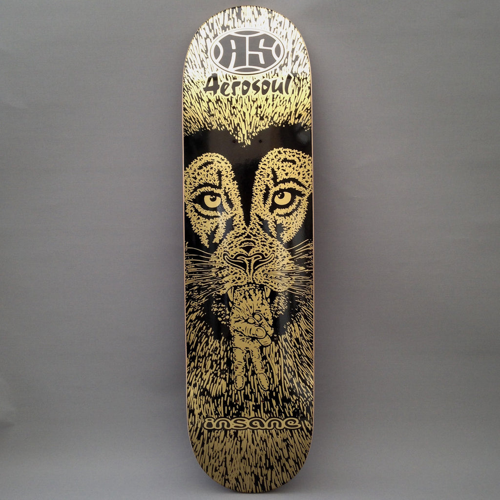 A skateboard deck featuring a black and gold graphic of a lions head Ged Wells graphic with the peace hand sign coming out of its mouth